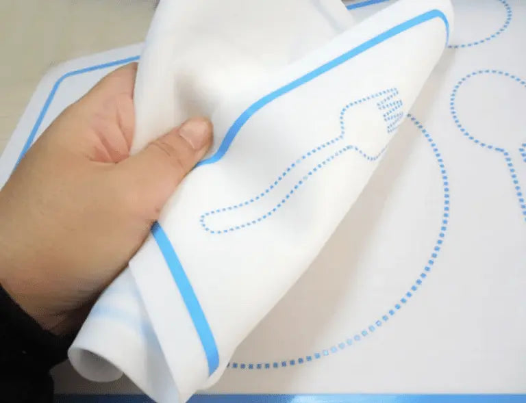 Une main tient un tapis de cuisine souple au charmant design de fourchette bleue, faisant écho à l'élégance pédagogique du Set de table montessori.