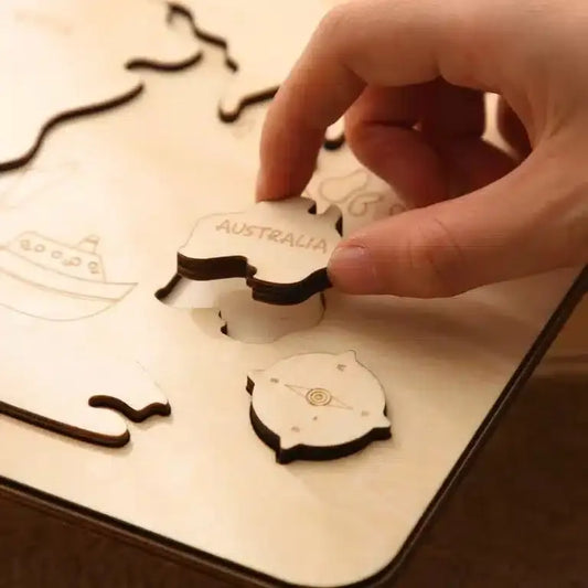 Une main place délicatement une pièce de puzzle en bois étiquetée « AUSTRALIE » dans le plateau Puzzle du monde en bois Montessori, avec une autre pièce à proximité.