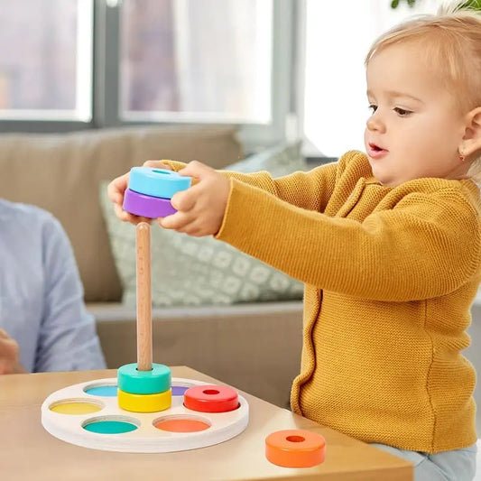 Un bébé joue avec un jouet coloré sur une table appelée "Jeu de Cercles à Enfiler".