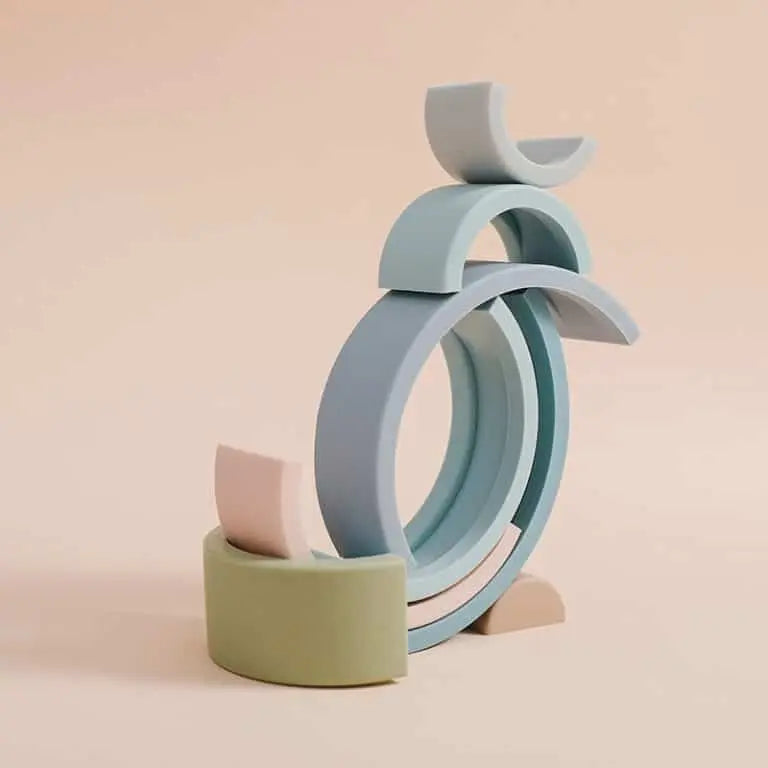 L'Arc en ciel Montessori en Silicone présente des demi-cercles et des arches empilés de couleur pastel, gracieusement équilibrés sur un fond beige.