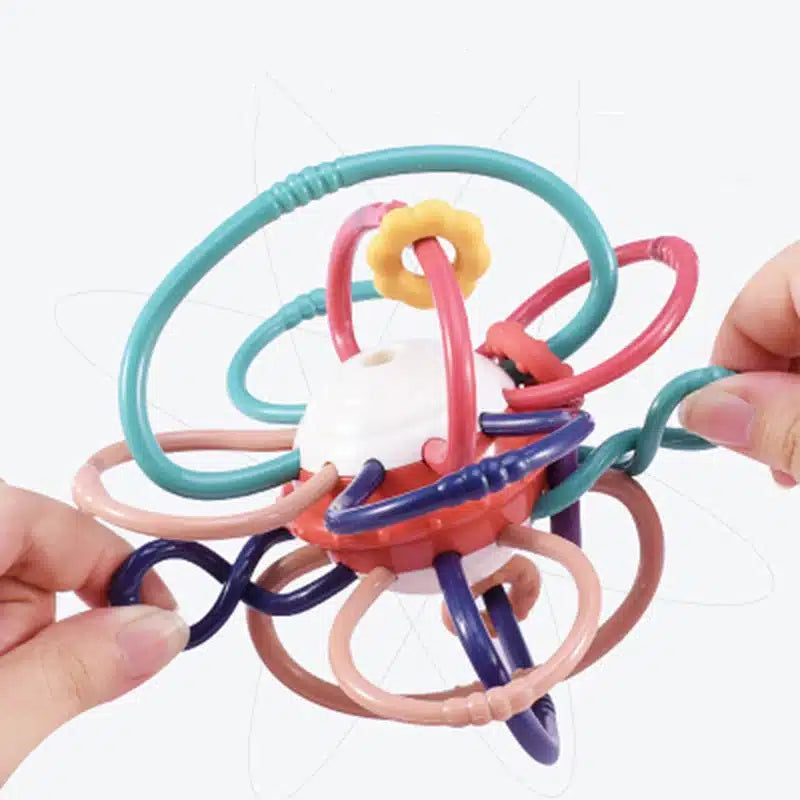 Les mains tiennent un jouet sensoriel Montessori pour bébé vibrant et à boucles multiples, comportant des anneaux interconnectés et une pièce blanche centrale, ressemblant au Hochet multi fonction- Montessori.