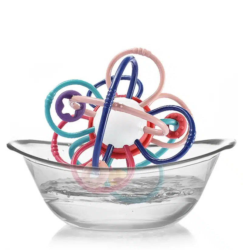 Le Hochet multi fonction- Montessori est un jouet vibrant qui flotte dans un bol en verre transparent rempli d'eau.