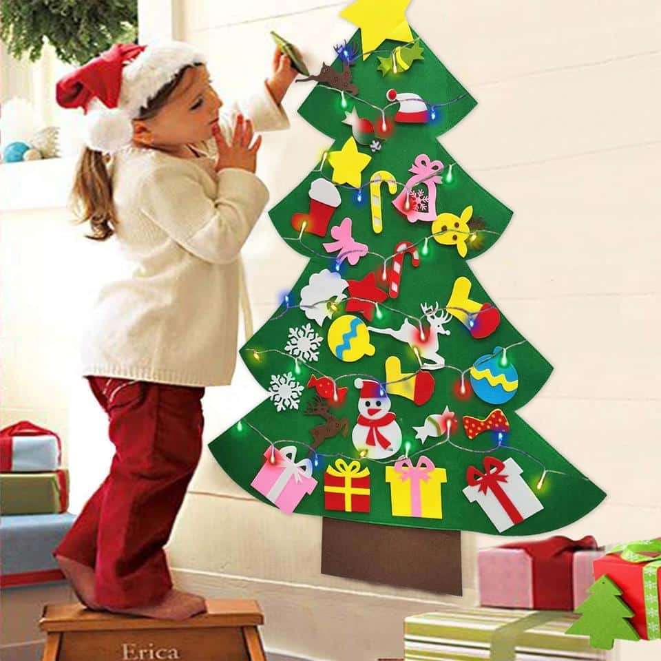 Une fille debout à côté d’un sapin de Noël festif en feutre avec 26 pièces décoratives.