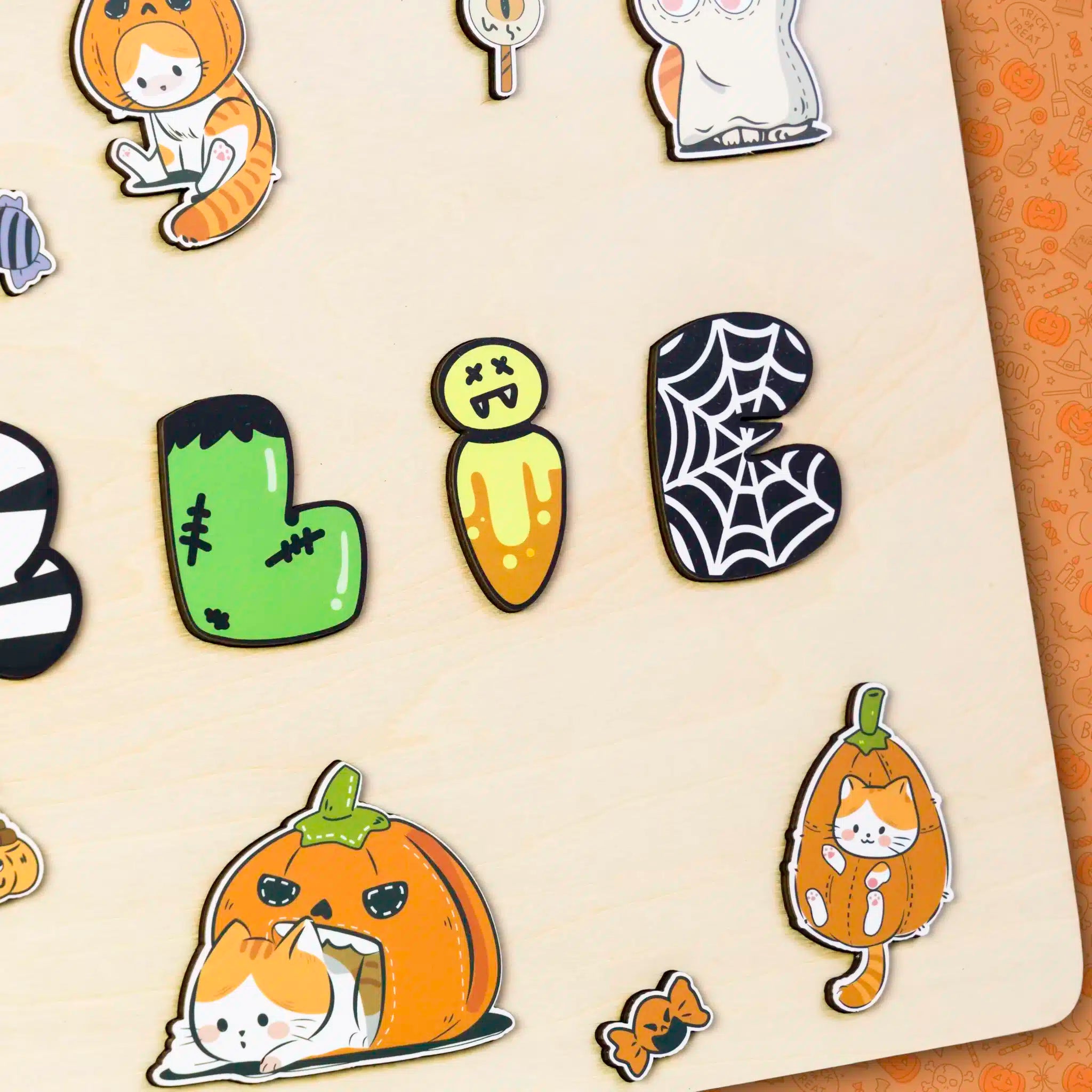 Des autocollants sur une planche présentant des motifs sur le thème d'Halloween, tels que des chats en costumes, des lettres de style monstre et un motif de toile d'araignée - un ajout délicieux pour toute collection de souvenirs Puzzle Personnalisé Prénom en Bois - Un souvenir unique (Copie) ou distinctive.