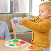 Un bébé joue avec un jouet coloré sur une table appelée "Jeu de Cercles à Enfiler".