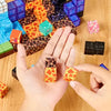 Quelqu'un dispose de petits blocs de mines à motifs de lave de « Mine Blocks - L'univers virtuel dans la vie réelle » sur une table en bois avec d'autres pièces colorées, fusionnant des thèmes virtuels avec la créativité de la vie réelle.