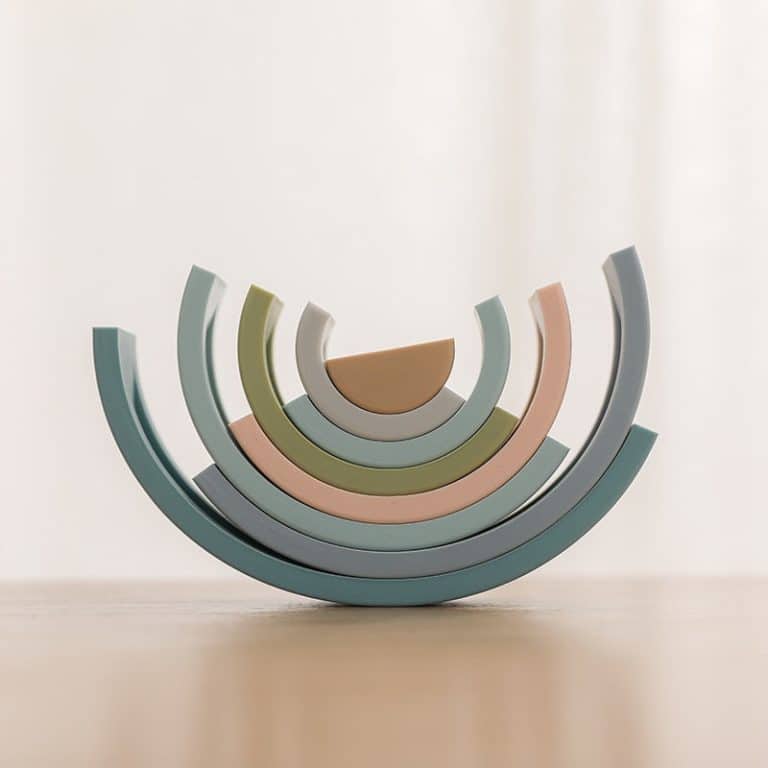 L'Arc en ciel Montessori en Silicone présente des demi-cercles pastel empilés sur une surface en bois avec un fond clair, évoquant une esthétique arc-en-ciel élégante et douce.