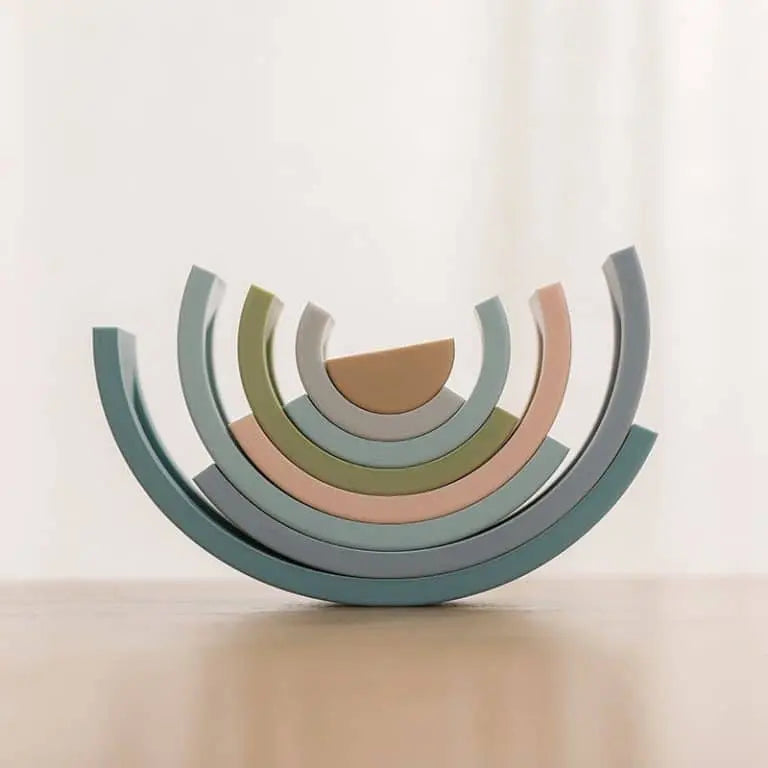 L'Arc en ciel Montessori en Silicone présente des demi-cercles pastel empilés sur une surface en bois avec un fond clair, évoquant une esthétique arc-en-ciel élégante et douce.