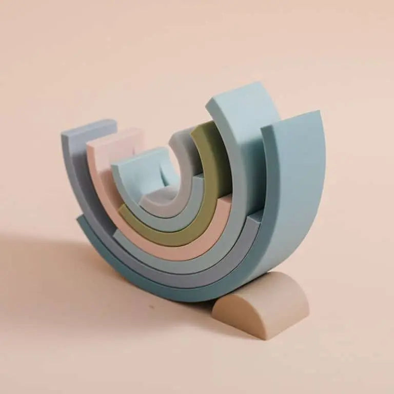 L'Arc en ciel Montessori en Silicone propose des blocs semi-circulaires aux couleurs pastel qui forment un arc-en-ciel abstrait sur un fond beige apaisant.