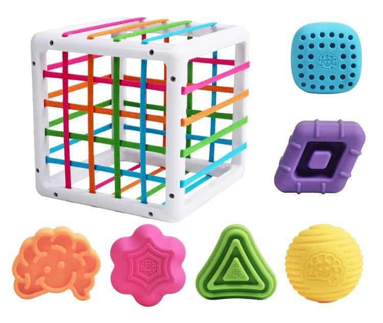 La Boite à formes avec élastiques – Jeu de motricité est un cube vibrant composé d'élastiques et de six formes texturées et multicolores aux motifs uniques pour une expérience ludique.