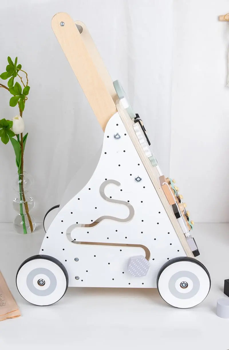 Un Trotteur pousseur bébé - multi-activités - Couleurs pastel est posé sur une table à côté d'un pot de fleur.